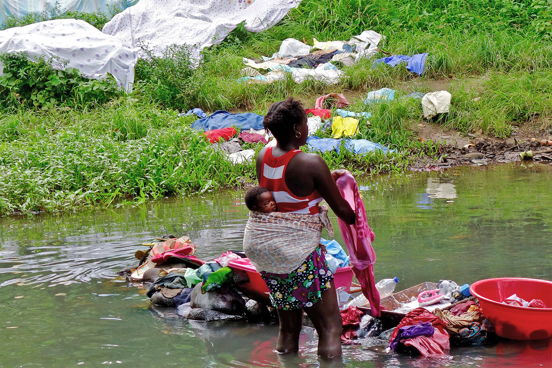 Uma mulher, com uma criança às costas, que lava a sua roupa no meio de um rio, é um bom exemplo na simplicidade das metas que nasce das intenções.