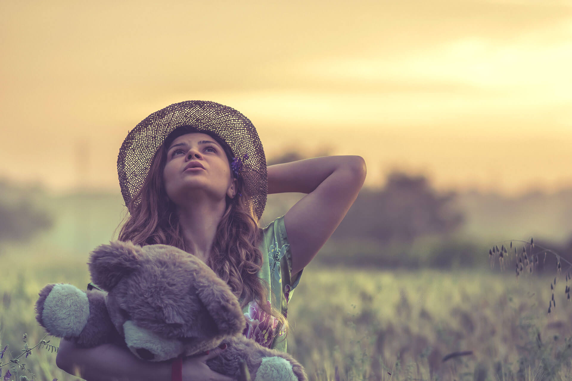 Rapariga com urso de peluche no campo, pelo pôr-do-sol