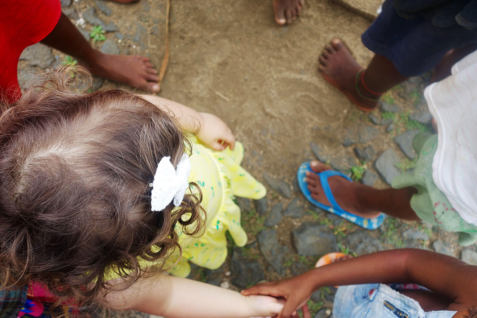Menina com laço branco no cabelo a brincar com crianças africanas.