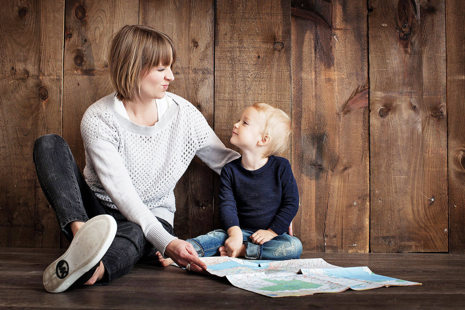 Mother and child sitting on the floor, leaning against the wood-lined wall and map on the floor.