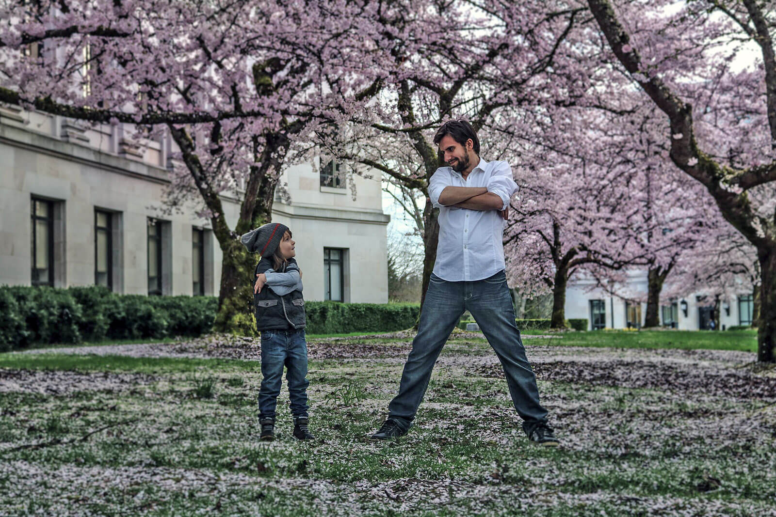 Pai e filho, de braços cruzados, num jardim com cerejeiras em flor.