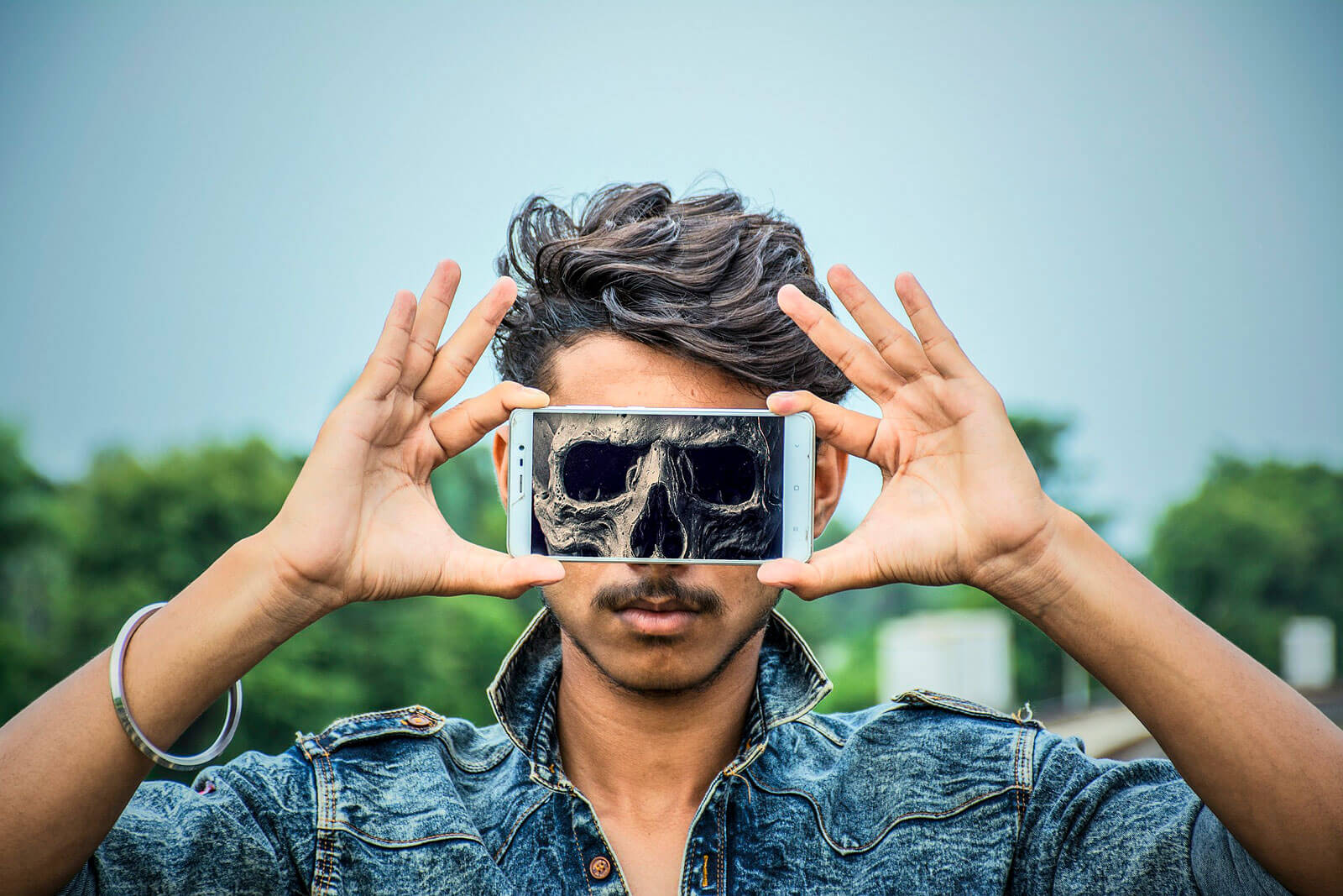 Boy with smartphone in the front of the his face, where you can see an image of a skull