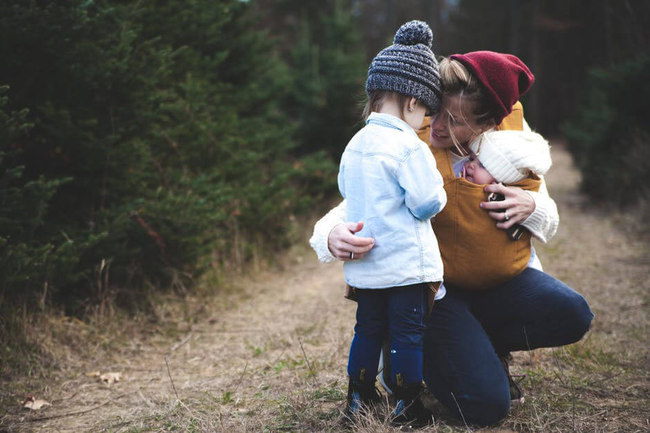 Mulher a abraçar duas crianças num caminho de um bosque.