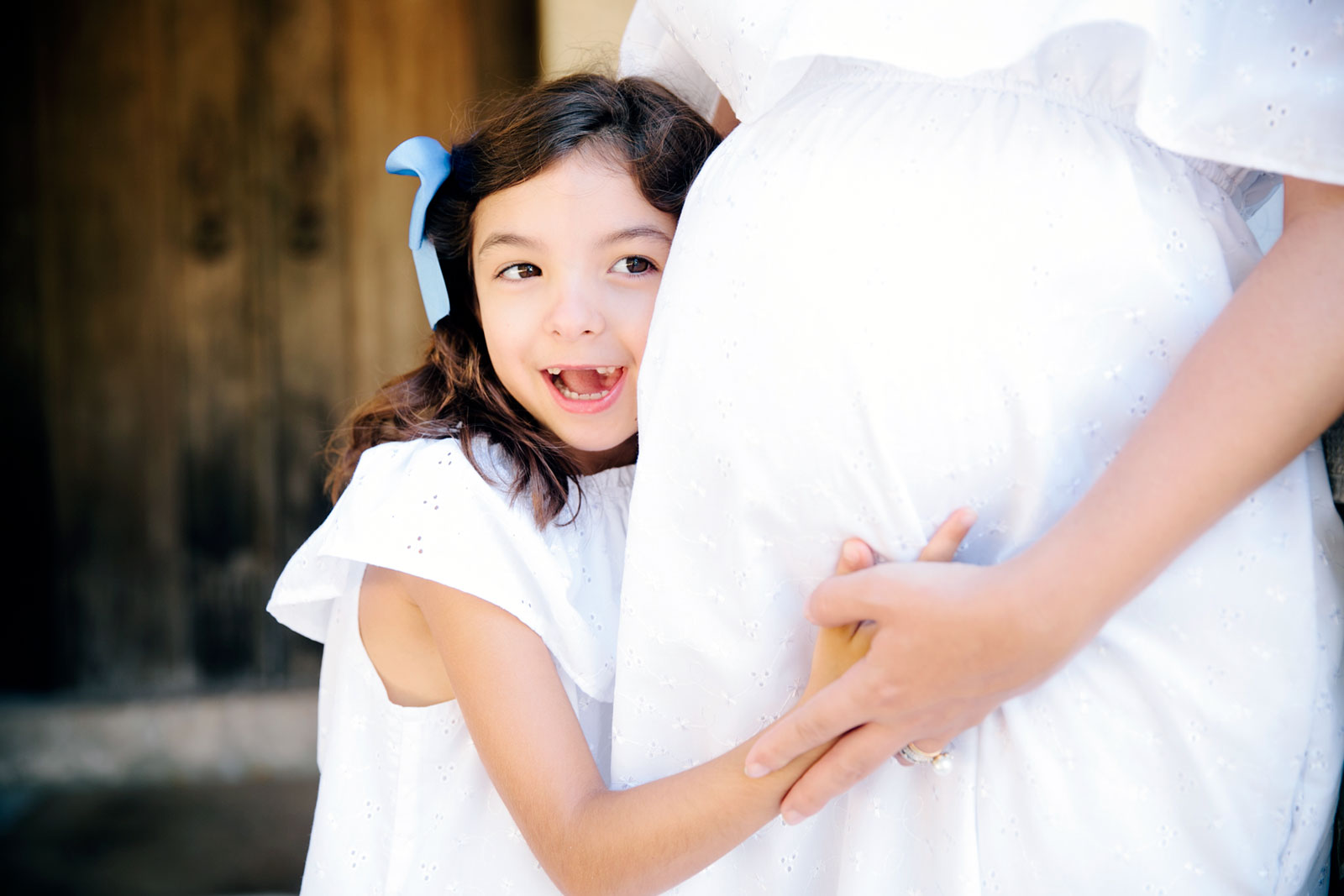 Criança a abraçar mulher grávida com vestido branco.