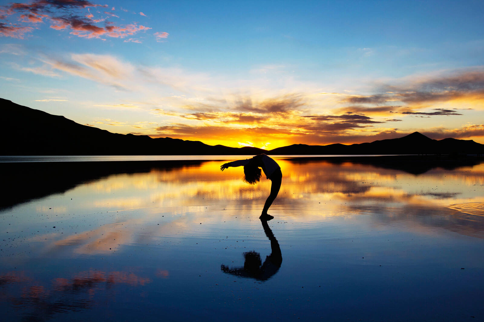 Mulher a fazer Yoga, numa praia ao pôr-do-sol