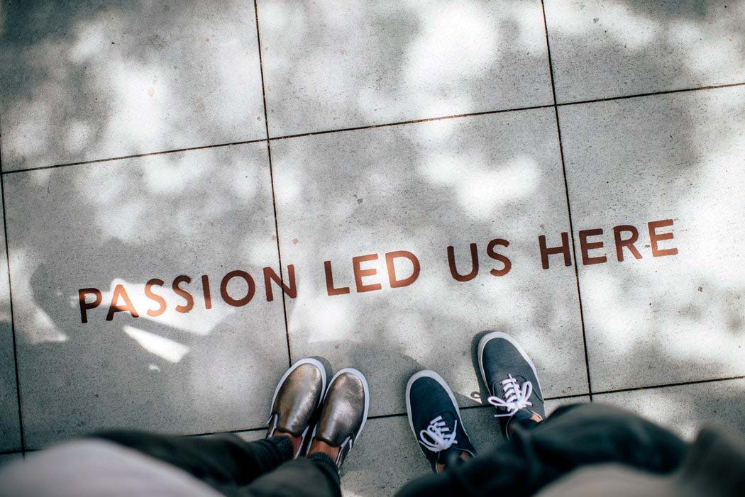 Pés sobre passeio, na rua, junto a inscrição "Passion led us here"