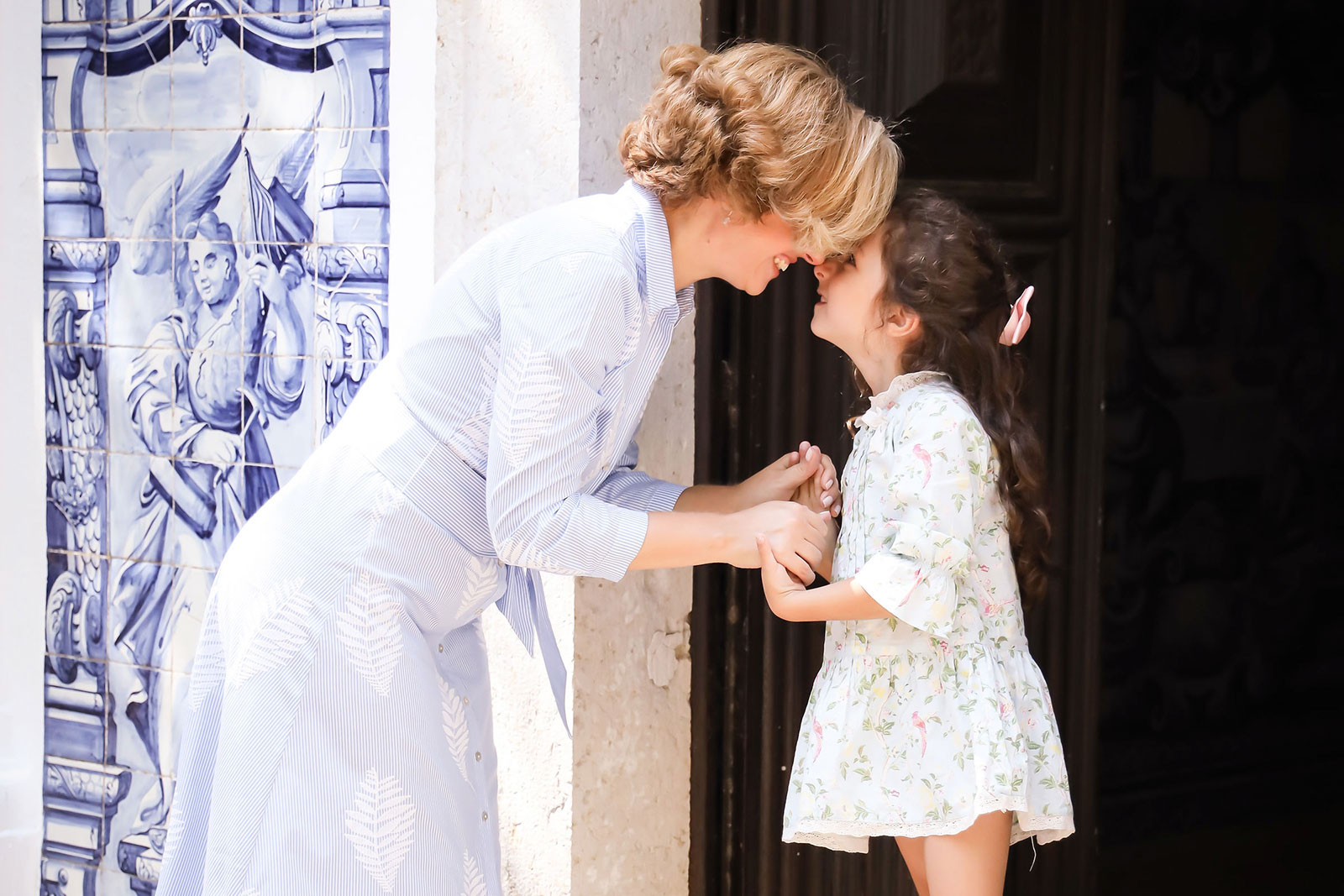 Rita Aleluia a segurar nas mãos de uma criança junto a uma igreja com azulejos azuis