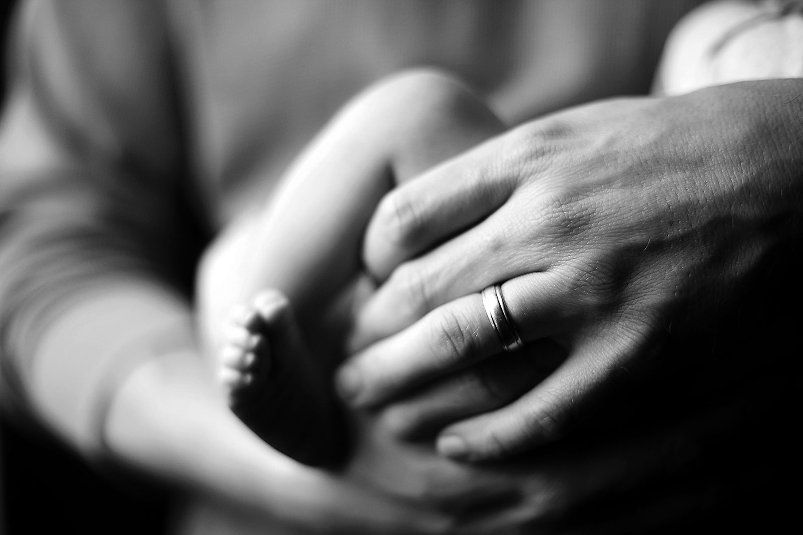 Homem, pai, com aliança no dedo da mão esquerda e bebé ao colo.